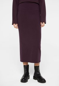 Dunkellila taillierte Midirock aus weichem Stoff, kombiniert mit schwarzen Knöchelschuhen mit dicker Sohle und runder Zehenpartie.