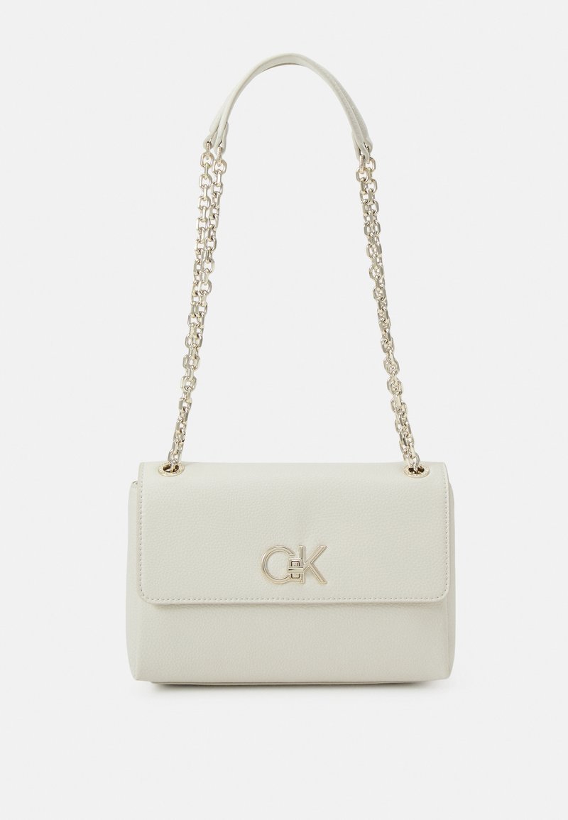 Petit sac à main beige clair avec fermeture à rabat, bandoulière chaîne dorée et logo métallique « CK » sur le devant.