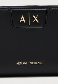 Black leather accessory with gold "A|X" logo and "Armani Exchange" text embossed on the surface.