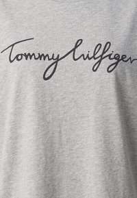 Lichtgrijze stof met handgeschreven stijl zwarte tekst "Tommy Hilfiger" die over het oppervlak is gedrukt.