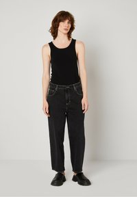Zwarte tanktop, hooglijn, losvallende zwarte spijkerbroek, standaard zakken, opgerolde mouwen, gecombineerd met zwarte instappers. Eenvoudig, casual ontwerp.