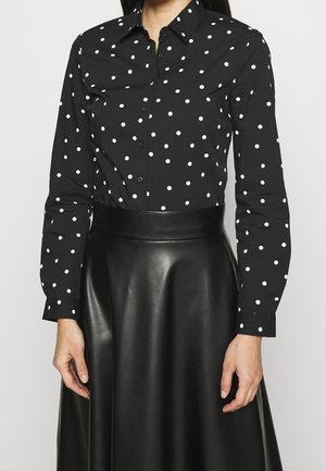 Sorte skjorte med hvide prikker, lange ærmer og krave, parret med en sort læderskirt med en flared design.