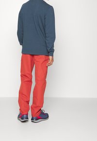Lange mouwen blauwe top, gecombineerd met feloranje broek en blauwe schoenen met rode accenten; gladde stof, relaxte pasvorm en rechte snit.