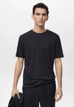 Mørkegrå crew-neck t-shirt med korte ærmer, lavet af et tekstureret stof, båret med mørke bukser og en matchende jakke.
