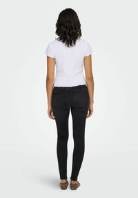 Valge soonikkoes lühikeste varrukatega topp, keha ümber istuv disain lõheservaga, kombineeritud mustade kitsaste teksadega. Modell seisab selg kaamerale pööratud.