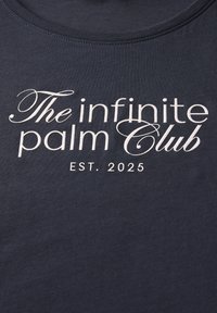 T-shirt bleu marine avec texte brodé blanc : "The infinite palm Club" et "EST. 2025", col rond, en coton doux.