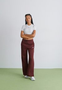 Vit Nike T-shirt, slim fit, i kombination med löst sittande, bordeauxfärgade sweatpants med dragsko och vit logotyp, fulländad med vita sneakers.