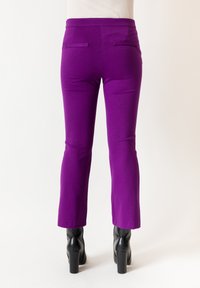 Pantaloni a zampa di elefante viola in tessuto elasticizzato, con una trama liscia, vita media e due tasche posteriori, abbinati a stivali neri con tacco largo.