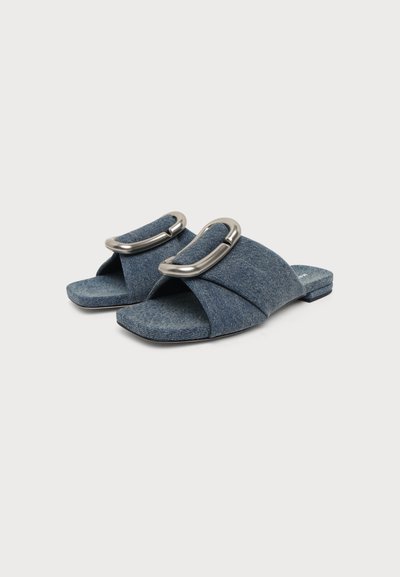 Μπλε denim σανδάλια με ανοιχτά δάχτυλα, φαρδιές υφασμάτινες λουρίδες και μεγάλες ασημένιες οβάλ αγκράφες, επίπεδες σόλες, σε λευκό φόντο.