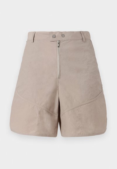 Pantaloni corti beige in un tessuto liscio e strutturato. Presentano una chiusura frontale con zip, due bottoni di fissaggio e dettagli di cucitura diagonale.