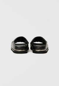 Pantofi negri tip slip-on din PVC neted, cu o talpă interioară texturată și un călcâi căptușit. Talpa exterioară are un accent argintiu contrastant.