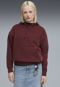 Bordeaux hætte sweatshirt med en frontlomme og et lille logo; sammen med en lys blå denimnederdel og solbriller stukket ind i taljen.