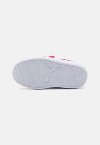 Suela de zapatilla blanca con sutiles patrones en forma de ola y un acento rosa en la parte superior; presenta un logo estampado en el centro. Superficie de agarre texturizada.