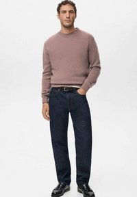 Jasnofioletowy dziergany sweter z prążkowanym dekoltem, w zestawieniu z ciemnoniebieskimi dżinsami i czarnymi butami. Prosty, klasyczny krój i design.