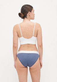 Hvit, ribbet bralette med tynne stropper sammen med blå, ribbede truser med hvit elastisk midje. Begge har en glatt tekstur.