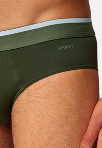 Groene katoenen slips met een lichtblauwe tailleband, voorzien van een platnaadontwerp en een subtiele logo aan de zijkant.
