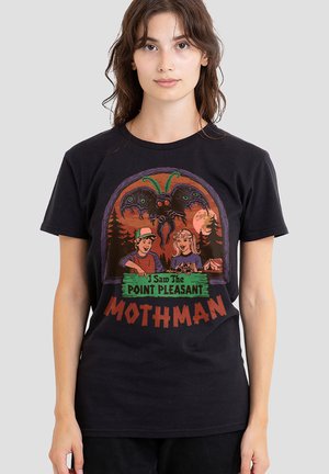 Young woman wearing a black t-shirt with colorful cartoon of kids, a large moth creature, and text "I Saw The Point Pleasant Mothman."