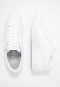 Ein Paar weiße Puma-Sneaker, wobei einer die Oberseite mit Schnürsenkeln und Logo innen zeigt, während der andere die Seite mit genähtem Design präsentiert.