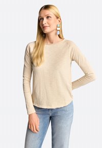 Beige pikkade varrukatega pluus ümmarguse kaelusega, lõdva istuvusega ja veidi kaardus äärtega. Ühendatud helesinine teksapüksid ja värvilised rippsõrmused.