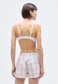 Λευκό σουτιέν με ρυθμιζόμεν ους ιμάντες και κούμπωμα με αγκράφα, σε συνδυασμό με ανοιχτόχρωμα καρό σορτς σε ροζ και άσπρες αποχρώσεις, με πίσω τσέπη.