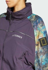 Purple lightweight jacket with high collar, featuring colorful galaxy-patterned sleeves and reflective accents. Logo on the chest and arm.