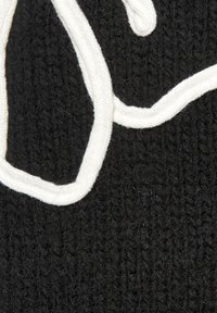 Schwarzer gestrickter Stoff mit einem weißen, erhabenen, strukturierten Muster, das an geschwungene Schrift erinnert. Das Material wirkt weich und zeigt sichtbare Fasern.