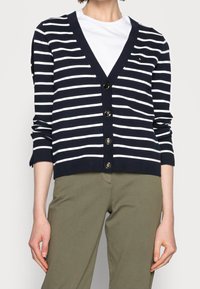 Marinblå och vitrandig cardigan med V-hals, 5 guldfärgade knappar och ribbade manschetter. Matchas med olivgröna byxor.