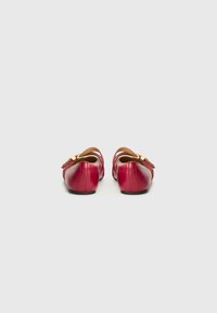 Ballerine in pelle rossa con finitura liscia, dotate di una cintura decorativa e hardware dorato. Punta arrotondata e tacco nero basso e solido.