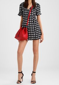 Sort kjole med hvidt hjerte-mønster, flæseærmer, parret med en rød spandtaske og sorte strophæle.