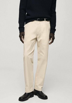 Mand iført cremefarvede bukser med lige ben, sort læderbælte, sort ribstrikket sweater og sorte læder Chelsea-støvler.