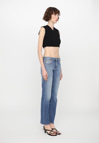 Black cropped top with scalloped edges, light blue straight-leg jeans with a slight fade, and black strappy heels. Model stands sideways.
