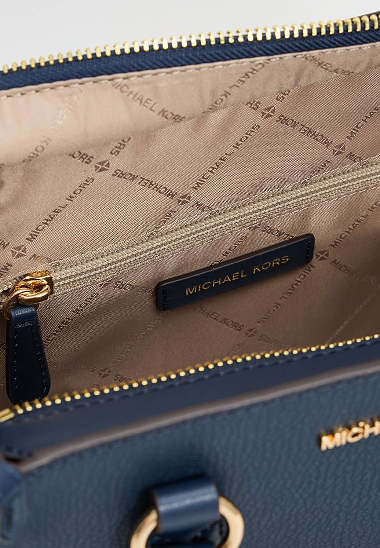 Interno di una borsa blu navy con pelle texturizzata. Caratterizzata da una cerniera dorata, foderatura in tessuto con marchio e un'etichetta. Visibili più scomparti.