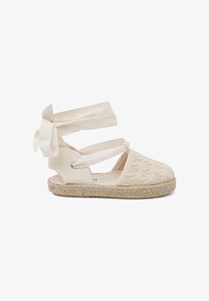 Sandale espadrille beige avec bout tissé, brides à nouer autour de la cheville, et semelle en jute tressée sur fond blanc.