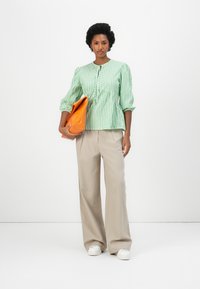 Πράσινο και λευκό ριγέ μπλουζάκι με φουσκωτά μανίκια, κουμπωτό μπροστινό μέρος και φούστα τύπου πεπλούμ. Συνδυασμένο με μπεζ παντελόνι σε φαρδιά γραμμή και πορτοκαλί τσάντα.