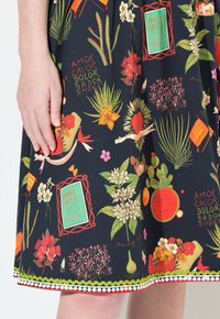 Schwarzes Stoffkleid mit lebendigen Blumen- und tropischen Mustern, ergänzt durch grüne, orange und rote Akzente; beinhaltet einen dekorativen Spitzenrand.