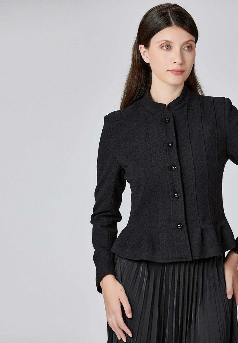 Veste noire cintrée avec un col haut, fermeture à boutons sur le devant et design plissé, en tissu texturé, assortie d'une jupe plissée.