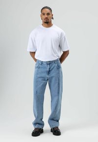 Witte T-shirt met korte mouwen, lichtblauwe losse jeans met contrasterend stiksel aan de zijkant en zwarte schoenen met een dikke zool. Eenvoudig ontwerp, geen patronen.