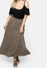 Top negro de hombros al aire combinado con una larga falda maxi en verde oliva, con volantes y una cinturilla elástica, acompañada de sandalias con tiras gruesas.