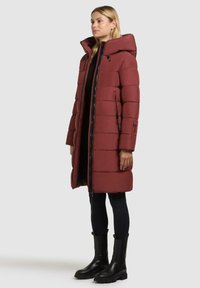 Bordeauxkleurige pufferjas met een capuchon, voorzien van een voordelige ritssluiting, zijzakken en een doorgestikt ontwerp. Gecombineerd met zwarte leggings en laarzen.