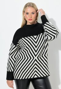 Svetr s černobílými pruhy a vzorem chevron, pletený materiál, oversized střih a vysoký límec. Nosený s černými koženými kalhotami.