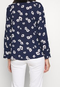 Námořnická blůza s dlouhými rukávy a květinovým vzorem v krémové barvě. Vyrobena z lehkého materiálu, má uvolněný střih a zaoblený lem.