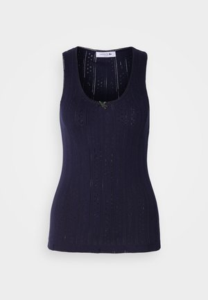 Sötétkék ujjatlan felső bordás textúrával, perforált részletekkel és mély nyakkivágással. Kicsi zöld díszítéssel készült.