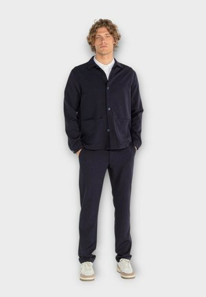 Veste bleu marine foncé avec deux poches avant, fermeture à boutons et pantalons assortis. Le tissu semble lisse avec une texture subtile et une coupe ajustée.