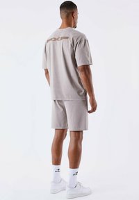 Conjunto de camiseta y pantalones cortos de algodón gris claro, con un logo en la parte posterior de un tono más oscuro. Combinado con zapatillas blancas y calcetines de diseño.