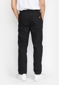 Zwarte katoenen broek met een elastische tailleband, rechte pijpen en een achterzak. Draag met witte sneakers.