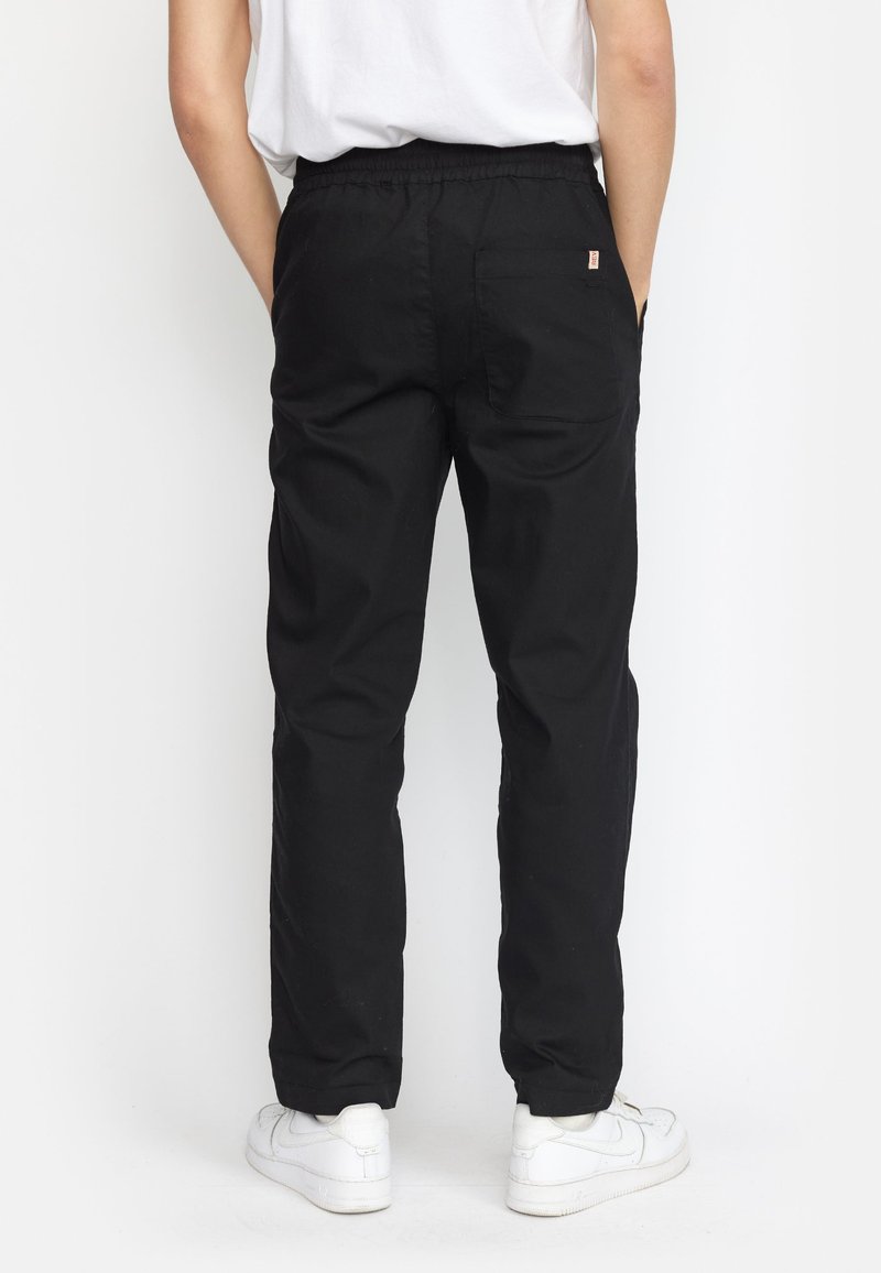 Zwarte katoenen broek met een elastische tailleband, rechte pijpen en een achterzak. Draag met witte sneakers.