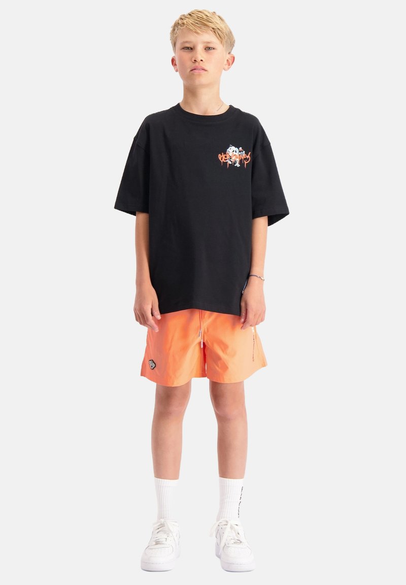Zwarte katoenen oversized t-shirt met grafisch ontwerp op de borst, gecombineerd met oranje zwembroek met zijzakken en logo-details. Witte sneakers.