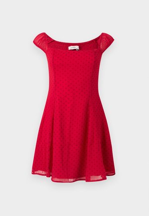 Sarkans kleita ar baltiem punktiņiem, ar īsām pūkainām piedurknēm, pieguļošu jostasvietu un izpletni svārkiem. Izgatavota no viegla auduma ar gludu tekstūru.