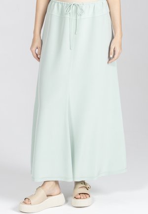 Kobieta ubrana w jasnozieloną, miętową spódnicę do kostek z regulowanym paskiem w talii oraz beżowe sandały na platformie z klamrami w kolorze złotym.