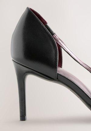 Juodos spalvos aukštakulnė basutė su blizgiu paviršiumi, atvira nugara ir plonu rožiniu dirželiu. Turi elegantišką siluetą ir siaurą stiletto kulną.